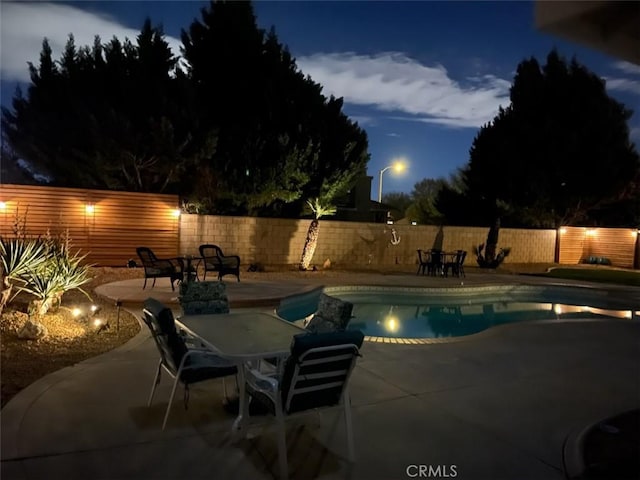 pool at twilight featuring a fenced backyard, outdoor dining area, a fenced in pool, and a patio