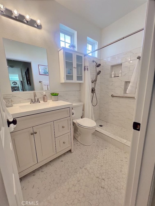 bathroom featuring tile walls, tiled shower, vanity, and toilet