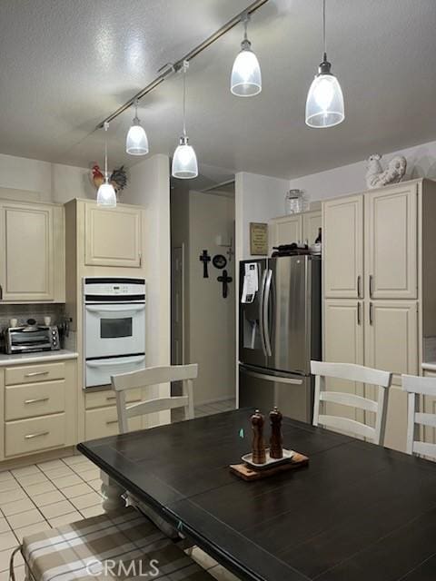 kitchen featuring stainless steel fridge with ice dispenser, white oven, cream cabinets, light countertops, and a warming drawer