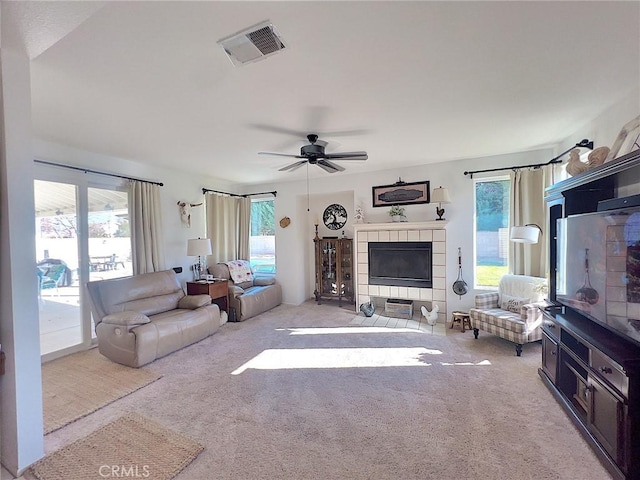 living area featuring a ceiling fan, a tile fireplace, visible vents, and light colored carpet