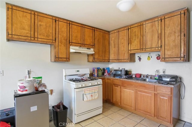 kitchen with brown cabinets, gas range gas stove, light tile patterned flooring, a sink, and under cabinet range hood