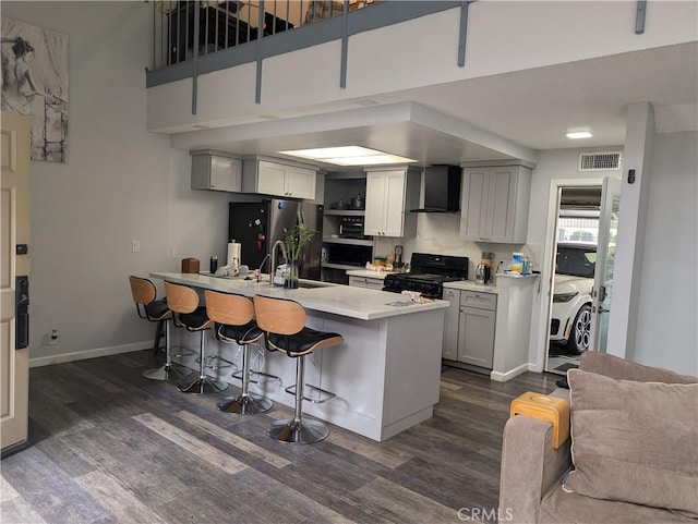 kitchen with a breakfast bar area, visible vents, wall chimney range hood, black range with gas stovetop, and freestanding refrigerator