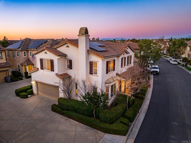 mediterranean / spanish home featuring a tile roof, a chimney, stucco siding, a residential view, and driveway