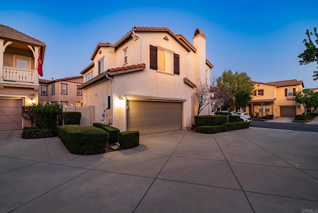 mediterranean / spanish-style house featuring an attached garage, a tile roof, concrete driveway, and stucco siding