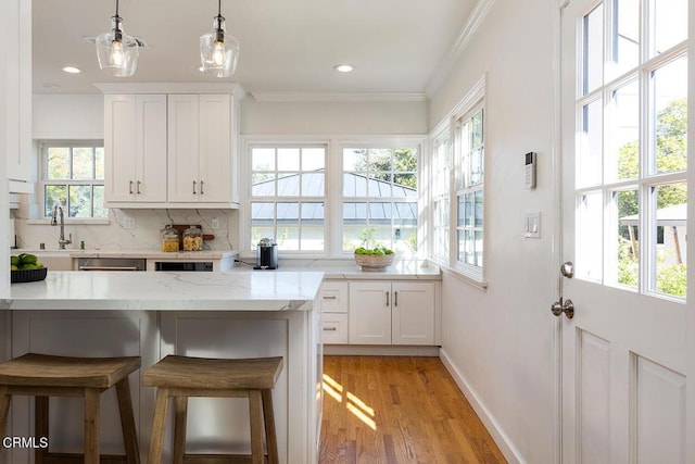 kitchen featuring a breakfast bar, light wood-style flooring, decorative backsplash, ornamental molding, and white cabinetry