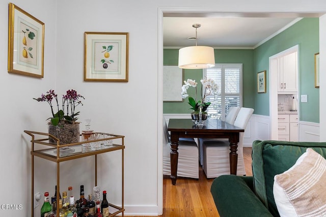 dining space featuring a wainscoted wall, ornamental molding, light wood-style flooring, and a decorative wall