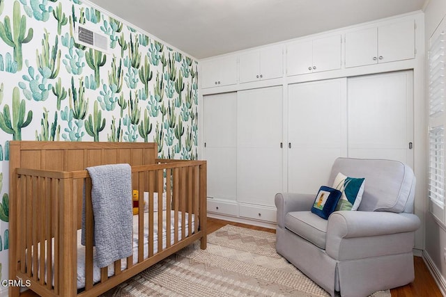 bedroom featuring a crib, wallpapered walls, light wood-style flooring, and a closet