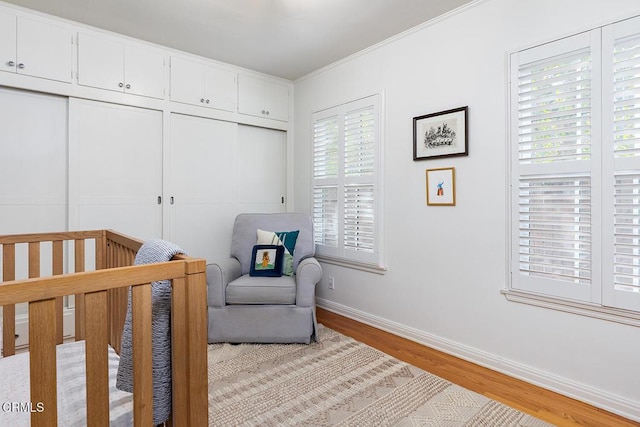 bedroom featuring a nursery area, a closet, baseboards, and wood finished floors