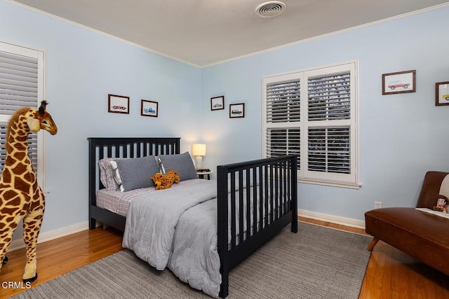 bedroom with baseboards, wood finished floors, visible vents, and crown molding