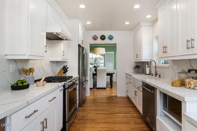 kitchen featuring white cabinets, high end appliances, custom range hood, light wood-type flooring, and a sink