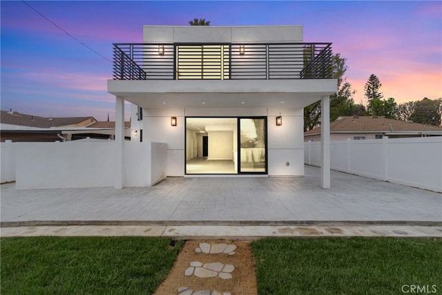 rear view of property featuring a patio area, a balcony, fence, and stucco siding