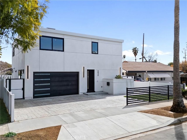 contemporary home featuring a fenced front yard, decorative driveway, an attached garage, and stucco siding