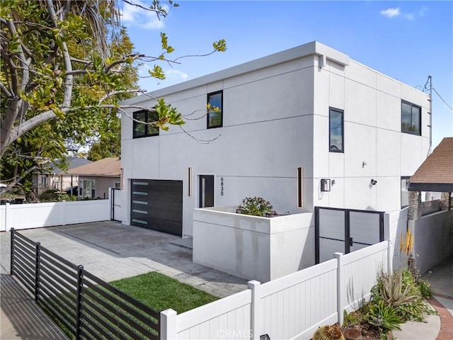 view of front of home with a garage, driveway, a fenced front yard, and stucco siding