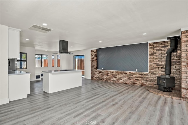 unfurnished living room with a wood stove, brick wall, visible vents, and wood finished floors