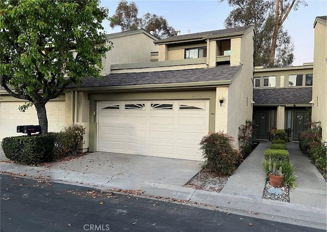 view of property with a garage, a shingled roof, concrete driveway, and stucco siding