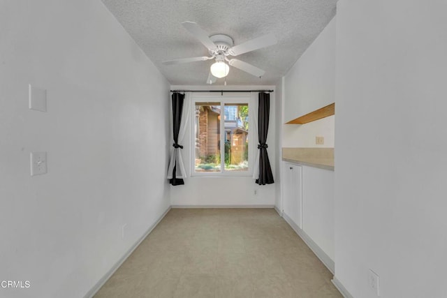 unfurnished room with light floors, baseboards, a ceiling fan, and a textured ceiling