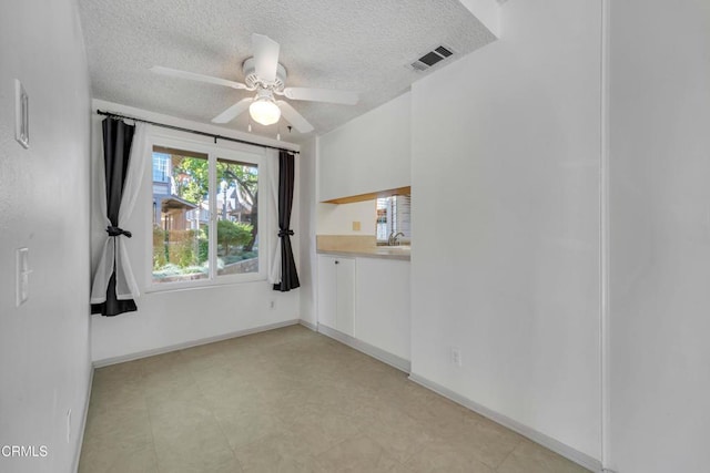 unfurnished room featuring baseboards, ceiling fan, visible vents, and a textured ceiling