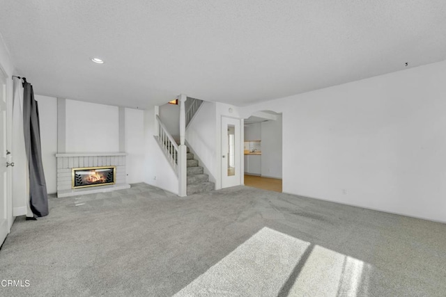 unfurnished living room with arched walkways, recessed lighting, carpet floors, a fireplace, and stairs