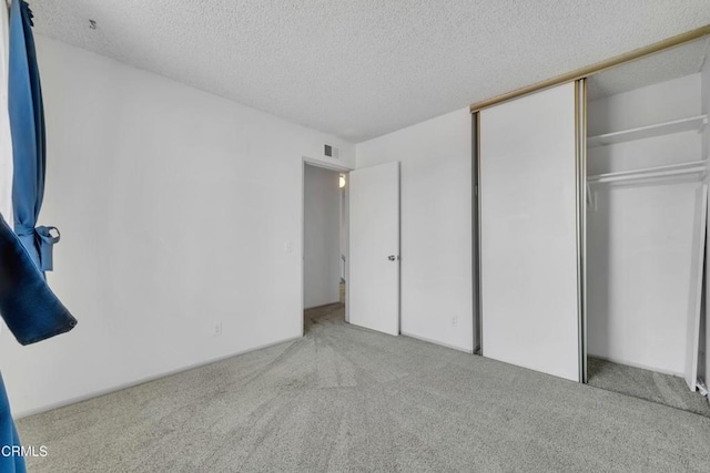 unfurnished bedroom with a textured ceiling, carpet floors, a closet, and visible vents