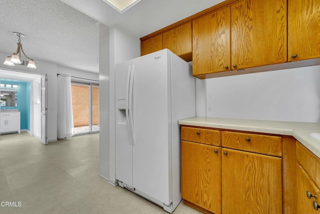 kitchen with white fridge with ice dispenser, brown cabinetry, light countertops, and a textured ceiling