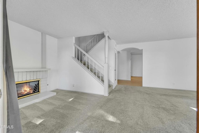 unfurnished living room with arched walkways, a textured ceiling, stairs, carpet, and a glass covered fireplace