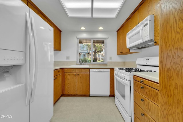 kitchen featuring brown cabinetry, white appliances, light countertops, and a sink