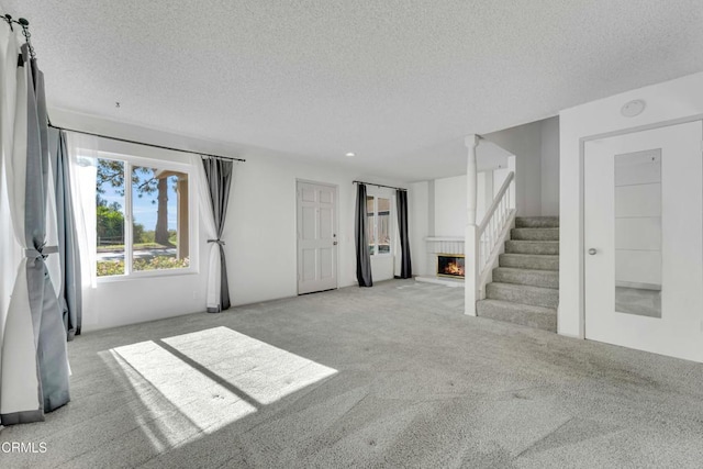 unfurnished living room featuring a glass covered fireplace, carpet flooring, stairway, and a textured ceiling