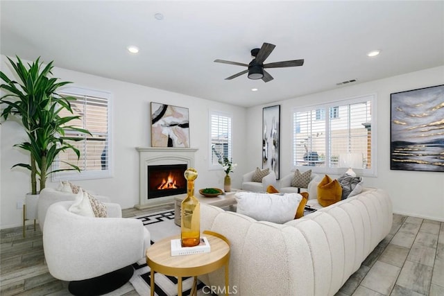 living room with a warm lit fireplace, light wood-style flooring, visible vents, and recessed lighting