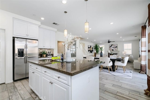 kitchen with white cabinets, dark stone counters, decorative backsplash, stainless steel fridge with ice dispenser, and a kitchen island