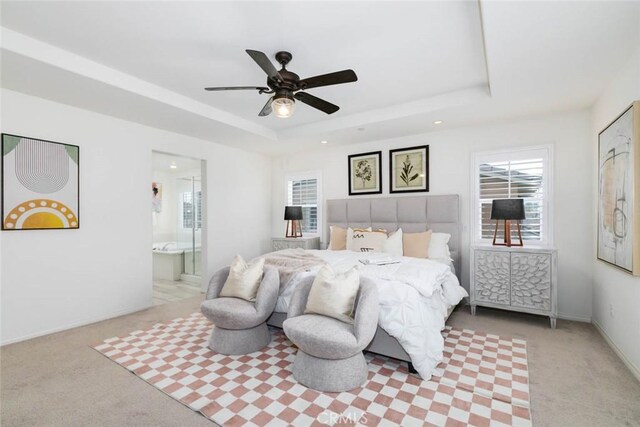 carpeted bedroom with ceiling fan, a tray ceiling, ensuite bath, and baseboards