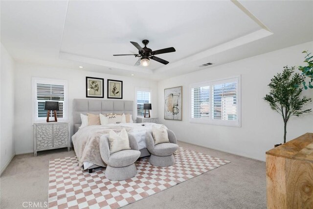 bedroom with a tray ceiling, visible vents, and light colored carpet