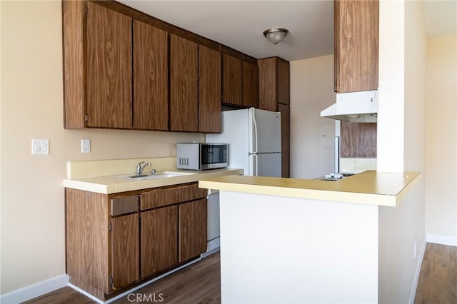 kitchen with a peninsula, dark wood-style floors, stainless steel microwave, and a sink