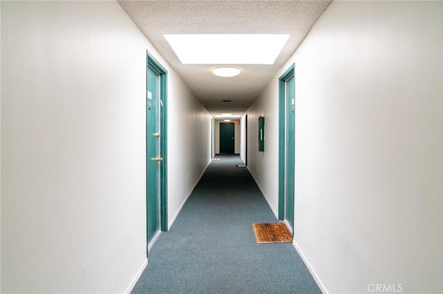 hallway with dark colored carpet, a skylight, and baseboards