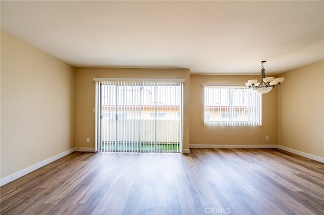 spare room with a chandelier, wood finished floors, and baseboards