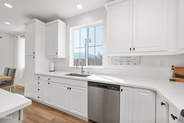 kitchen featuring white cabinets, dishwasher, light countertops, light wood-type flooring, and a sink