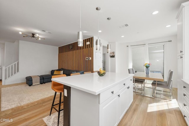 kitchen with white cabinetry, light wood-type flooring, visible vents, and a center island