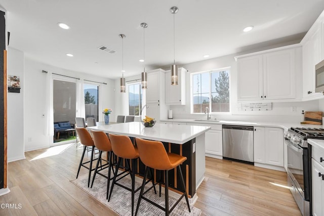 kitchen featuring a breakfast bar area, stainless steel appliances, visible vents, light wood-type flooring, and a center island