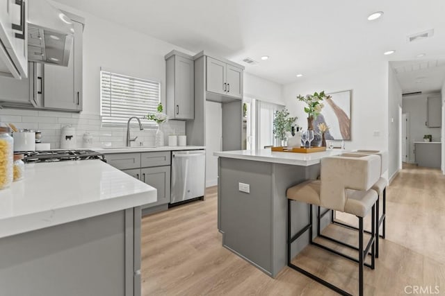 kitchen featuring gray cabinetry, a breakfast bar, a sink, light countertops, and stainless steel dishwasher