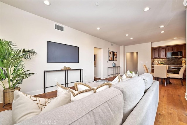 living area with visible vents, baseboards, light wood-style flooring, and recessed lighting