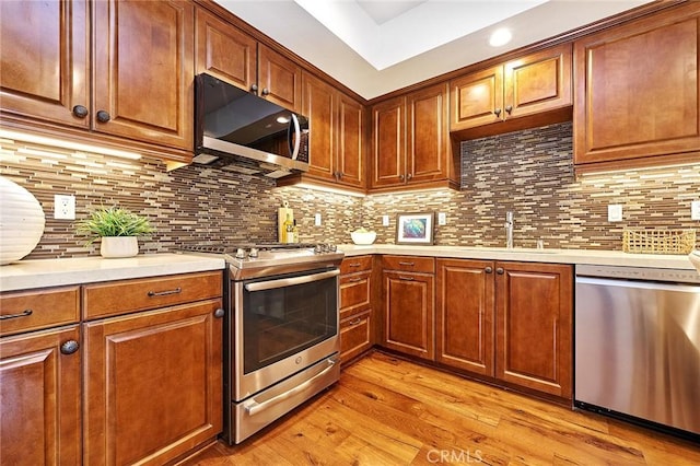 kitchen featuring a sink, light wood-style floors, light countertops, appliances with stainless steel finishes, and decorative backsplash