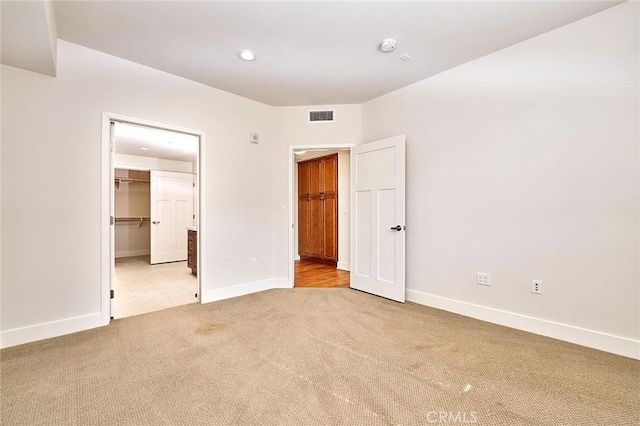 unfurnished bedroom with carpet, visible vents, a spacious closet, and baseboards