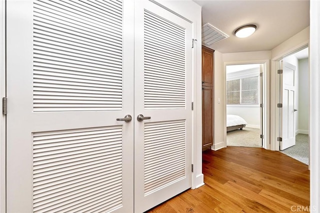 hallway featuring light wood-style flooring, visible vents, and baseboards