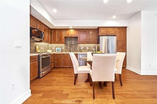 kitchen featuring stainless steel appliances, backsplash, light wood-style flooring, and baseboards