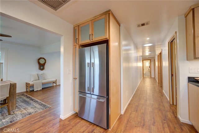 hall featuring light wood-style floors, baseboards, visible vents, and ornamental molding