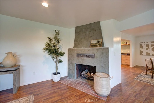 living area with a large fireplace, baseboards, and wood finished floors