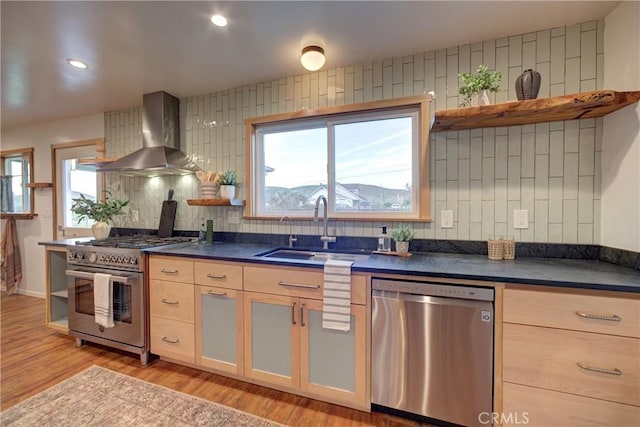 kitchen featuring dark countertops, wall chimney range hood, stainless steel appliances, and a sink