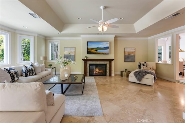 living area with crown molding, a raised ceiling, visible vents, a glass covered fireplace, and baseboards