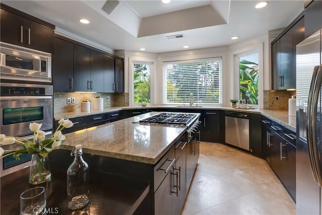 kitchen with stainless steel appliances, a sink, visible vents, light stone countertops, and a tray ceiling