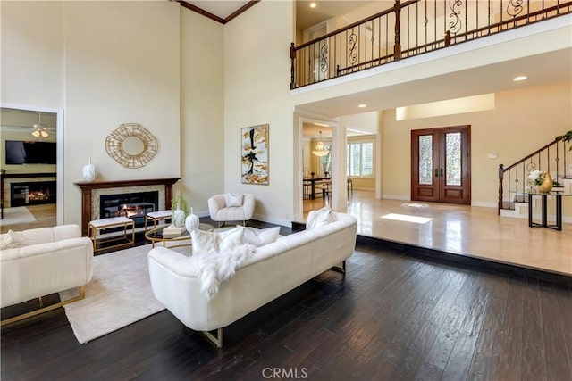 living area with baseboards, a glass covered fireplace, stairway, ornamental molding, and dark wood-style flooring