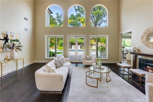 living room featuring french doors, dark wood-style flooring, a tiled fireplace, and baseboards